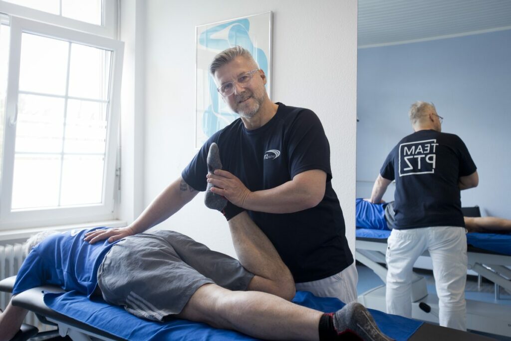 Physiotherapeut mobilisiert das Bein eines Patienten auf der Therapieliege
